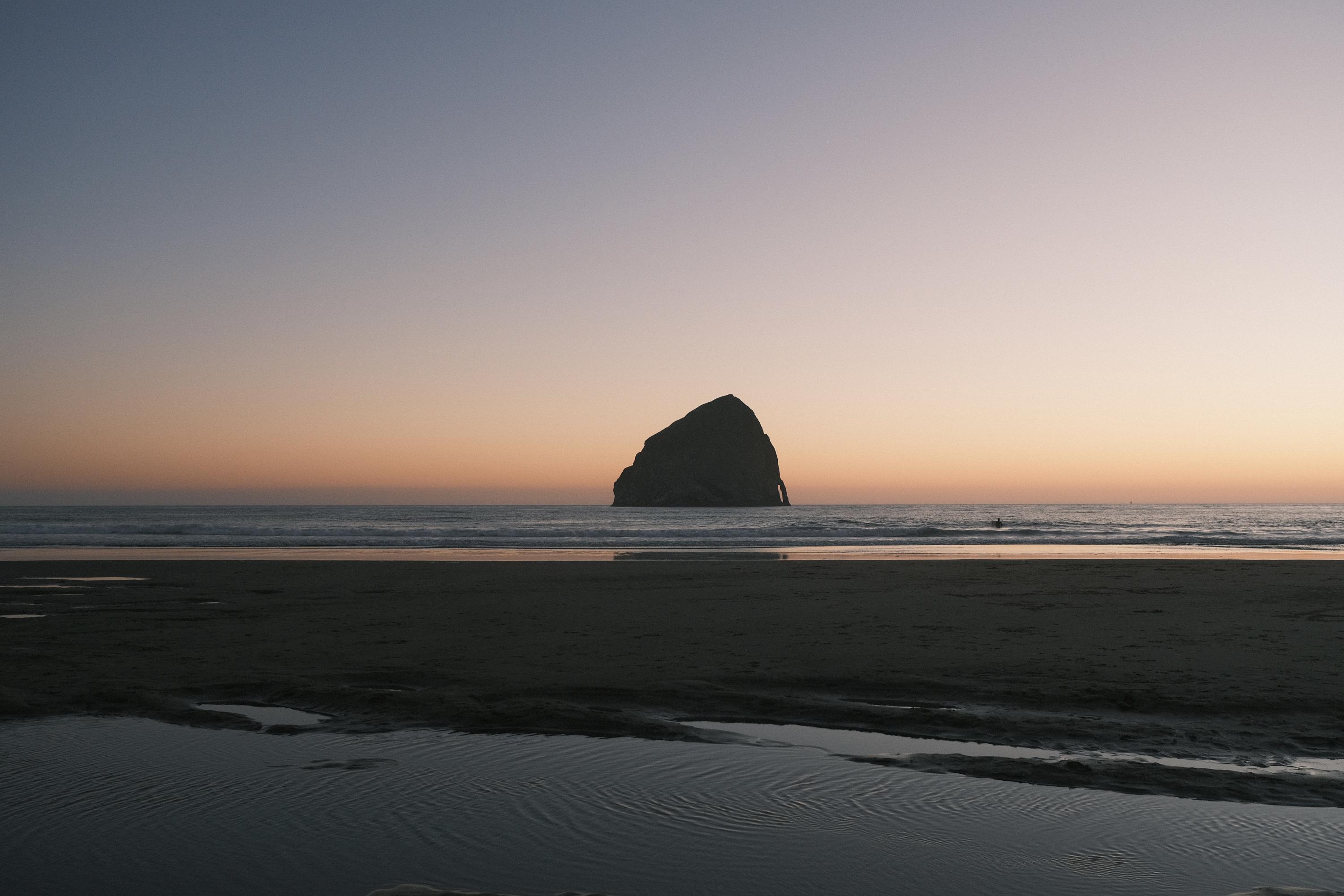 A great haystack rock on the oregon coast during sunset, with the tide rolling out and revealing the sand